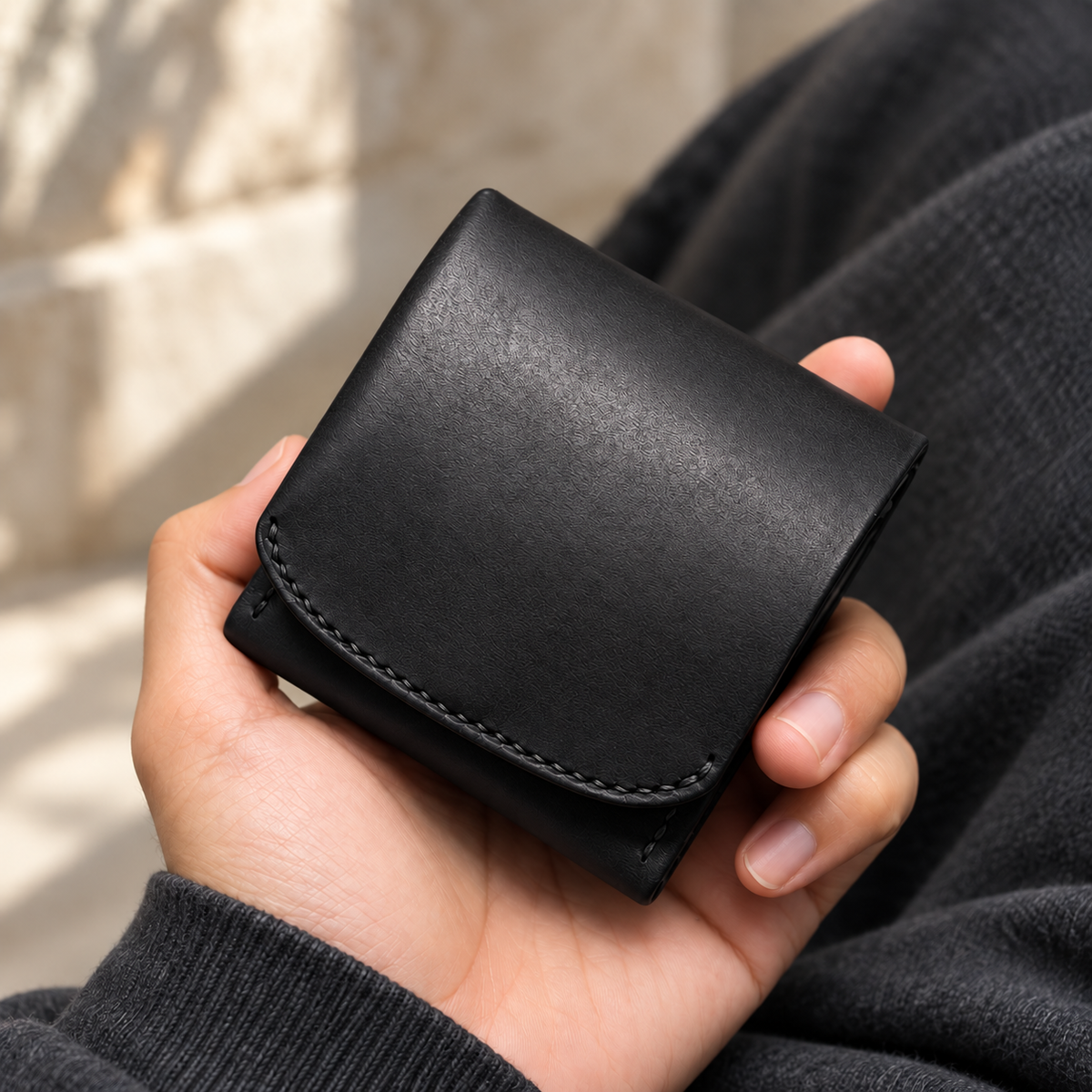 Black foldover wallet with black stitching held in one hand