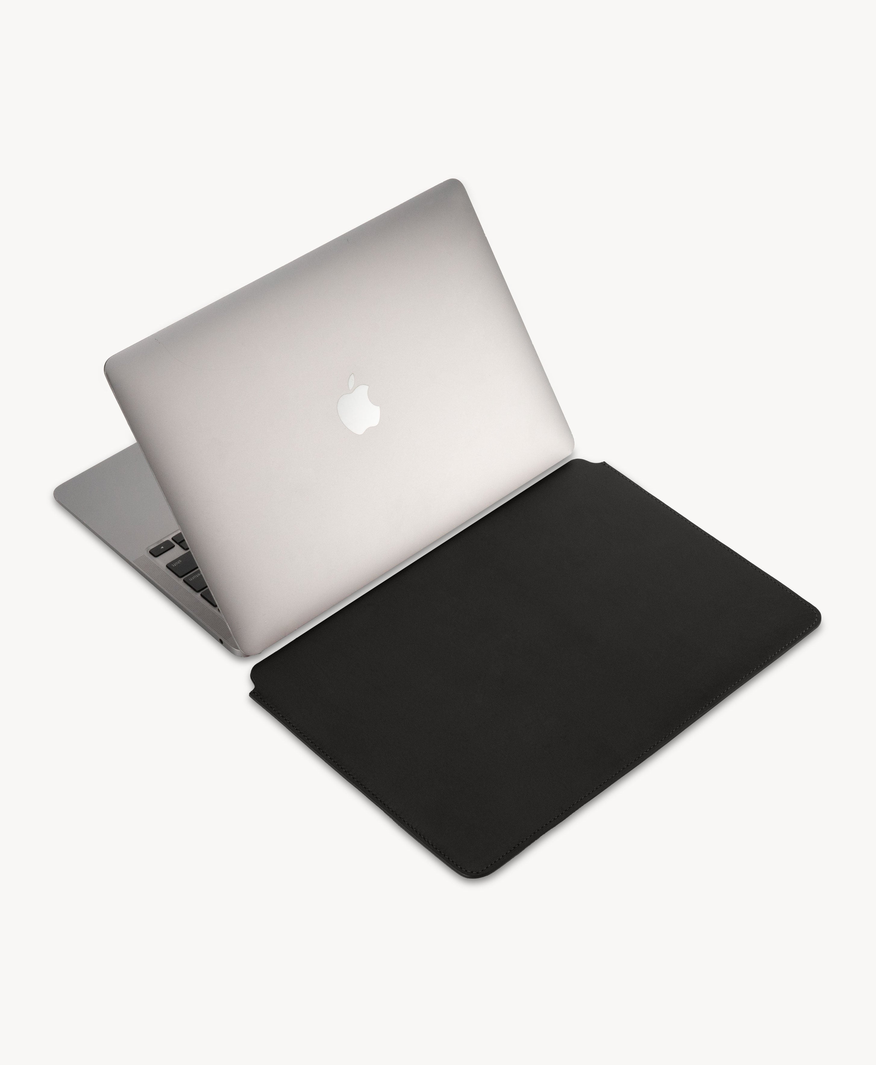 Black full grain saddle leather laptop sleeve, beside an open MacBook