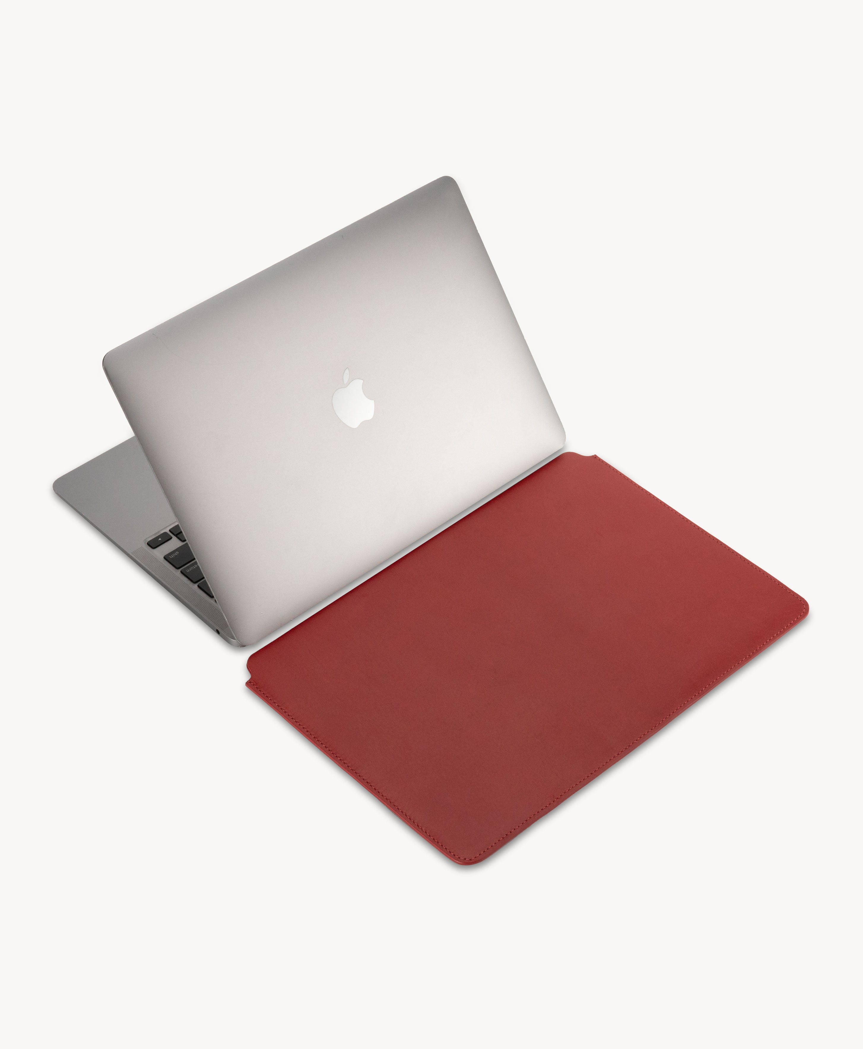Red full grain saddle leather laptop sleeve, beside an open MacBook
