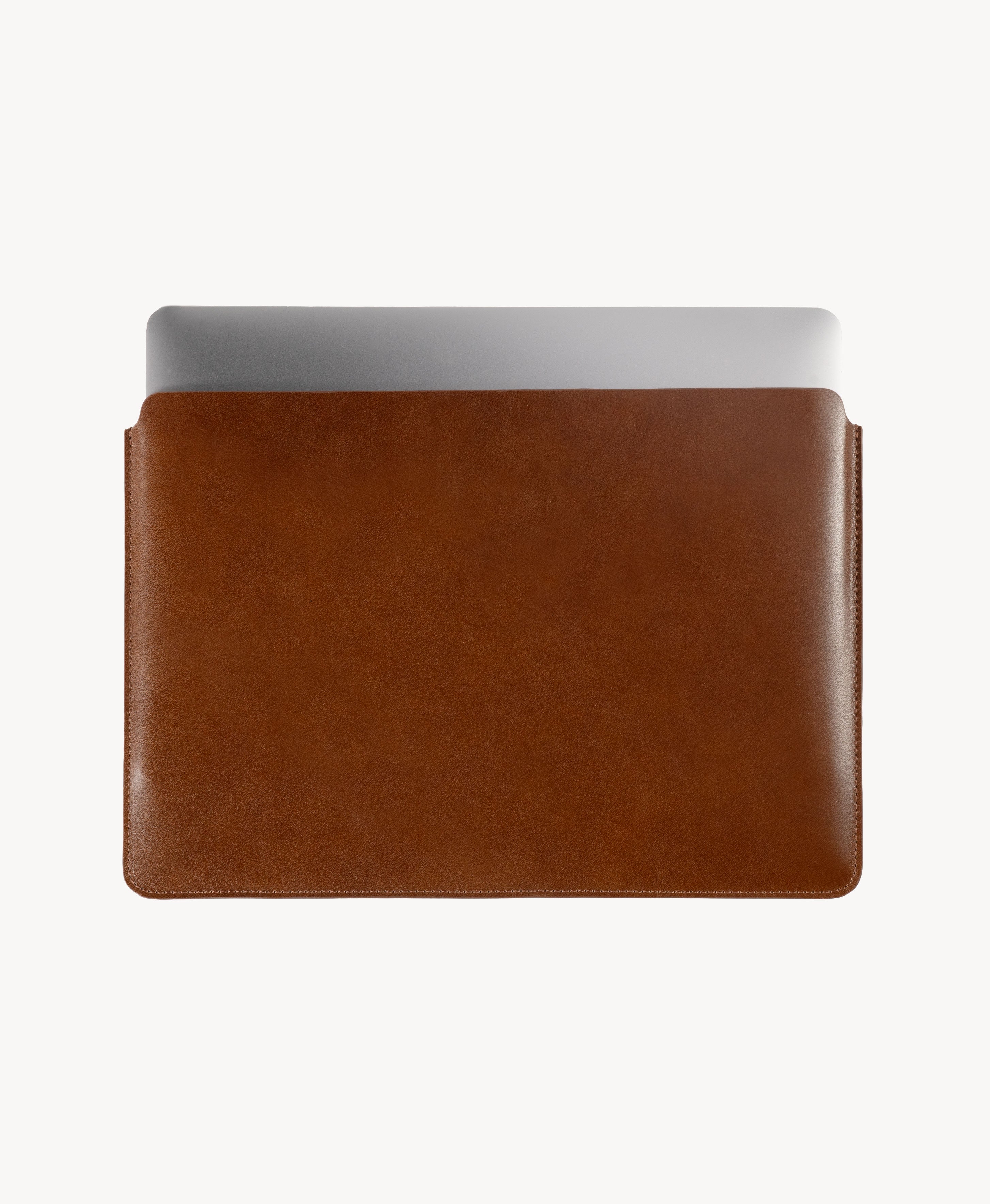 Brown full grain saddle leather laptop sleeve, MacBook partially inserted through the open top