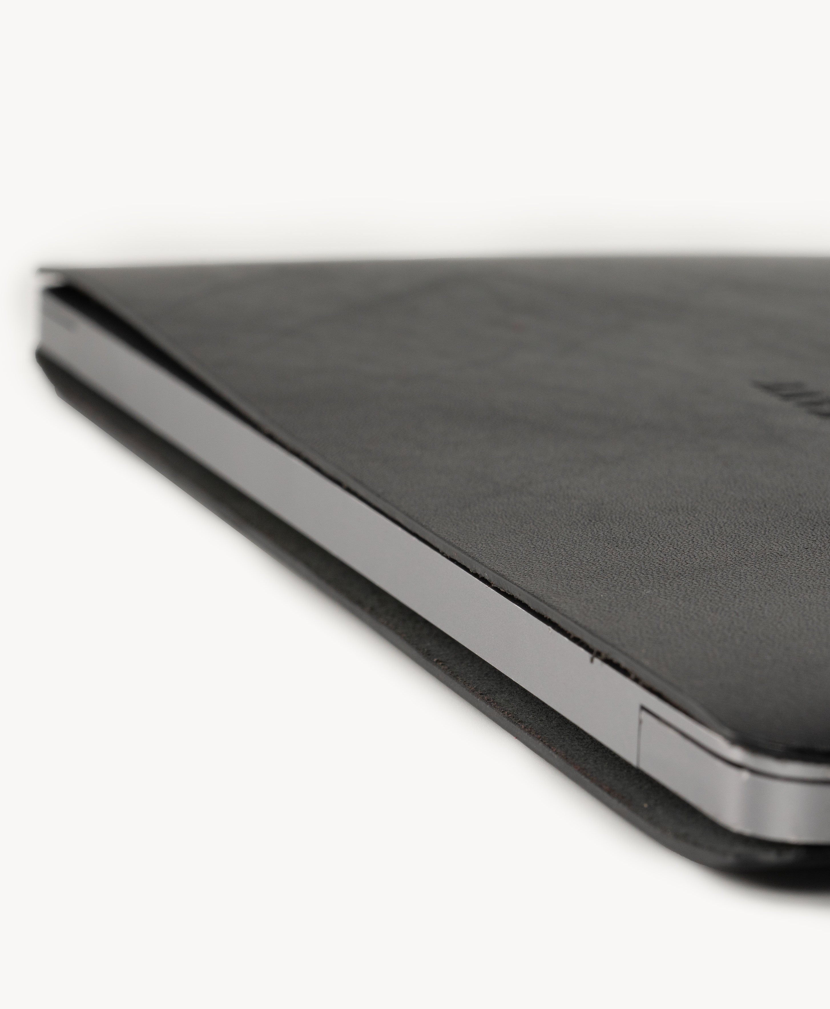 Black full grain saddle leather laptop sleeve, slim side profile with a MacBook inserted