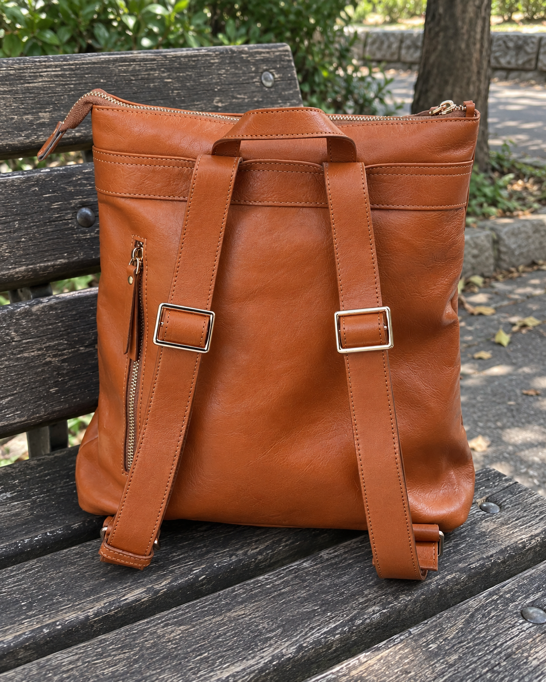 AI-generated lifestyle image showing the back of the orange leather backpack, adjustable straps and buckles on a park bench