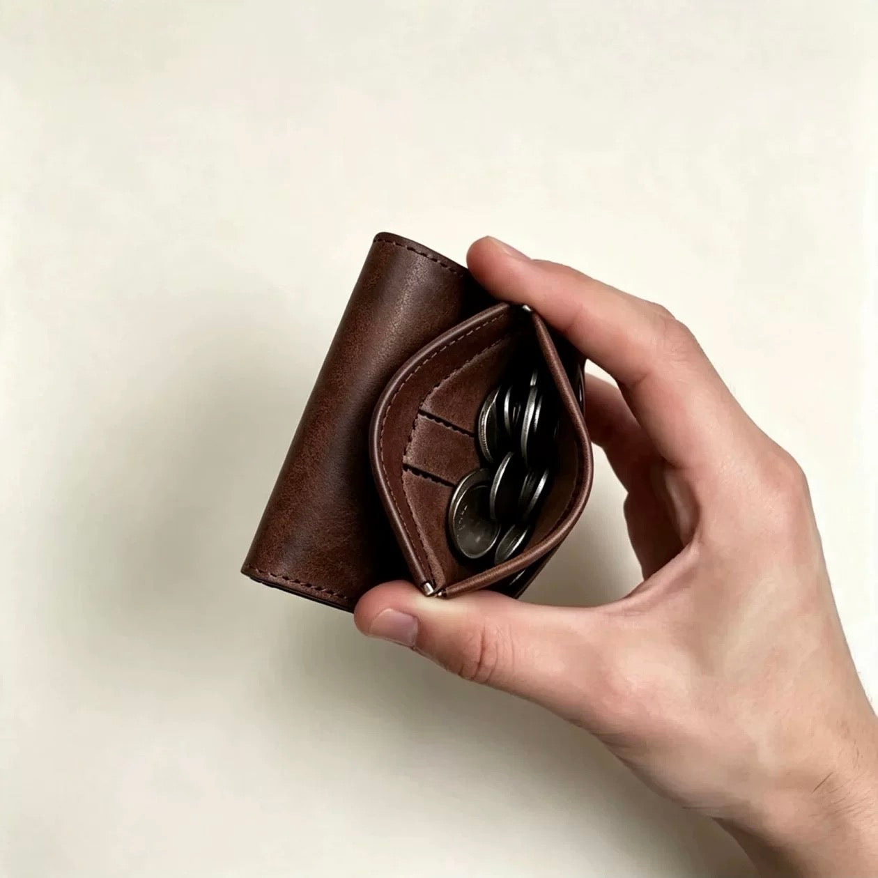 Brown full-grain leather trifold wallet with dedicated coin pocket in hand