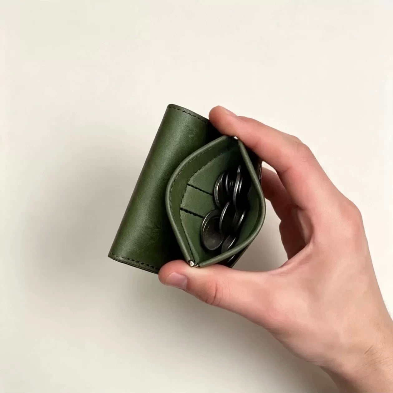 Green full-grain leather trifold wallet with dedicated coin pocket in hand